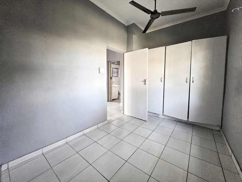 A vacant bedroom featuring tiled flooring, built-in cupboards, and a ceiling fan, with direct access to an adjoining bathroom.