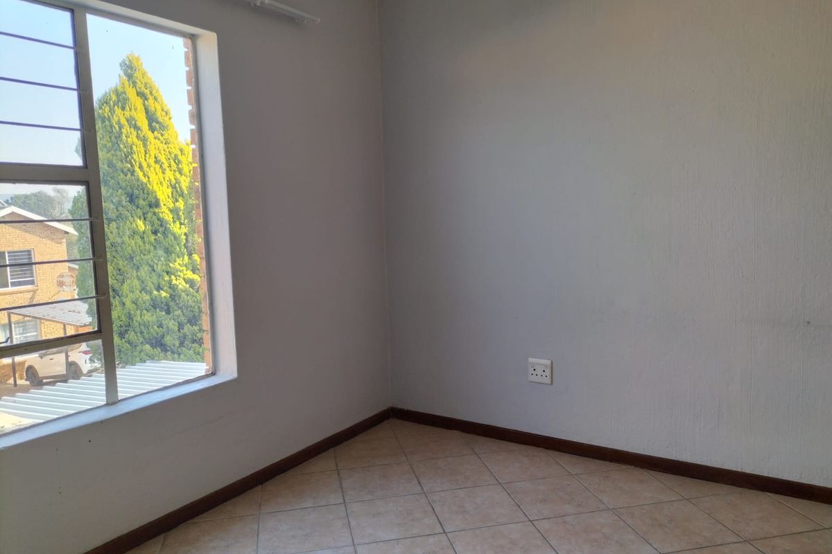 An empty bedroom featuring neutral wall paint, tiled flooring, and a window with security bars, offering a clean and versatile space.