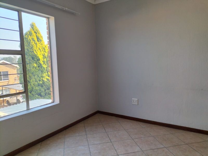 An empty bedroom featuring neutral wall paint, tiled flooring, and a window with security bars, offering a clean and versatile space.