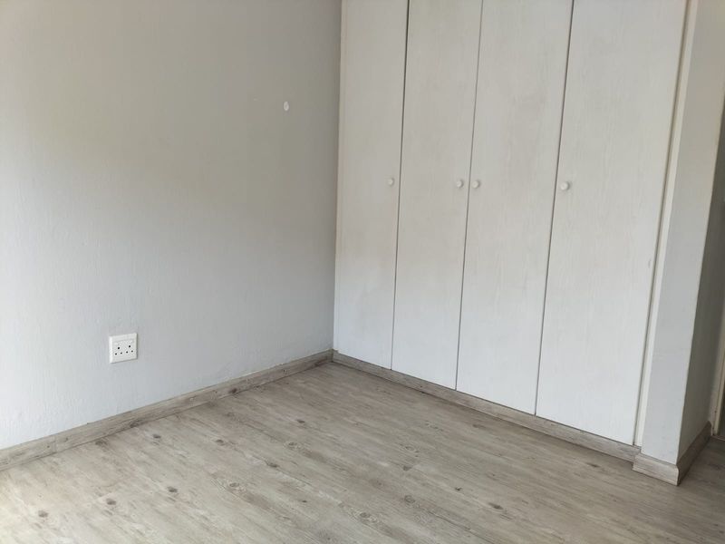 A clean, empty bedroom featuring light-toned laminate flooring and white built-in cupboards, providing a neutral canvas for personalization.