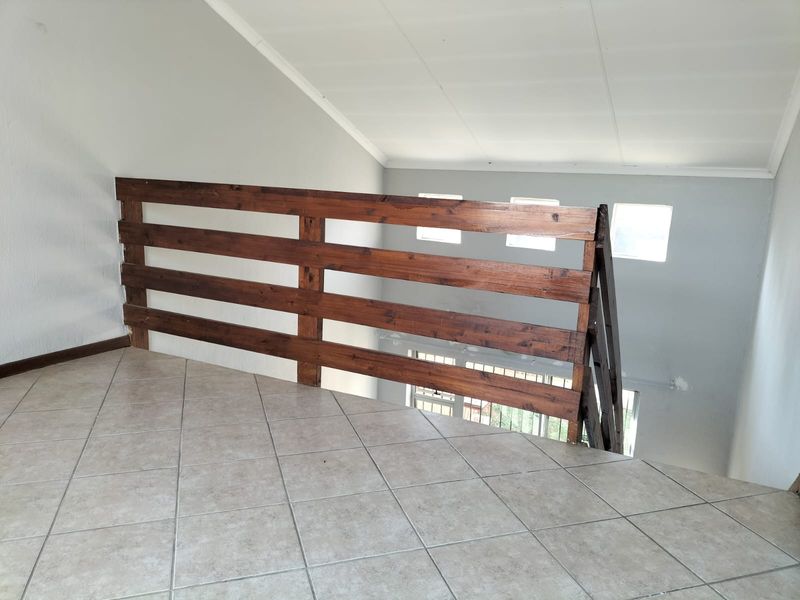 An open mezzanine landing area featuring tiled flooring, a wooden balustrade, and a vaulted ceiling with natural light from skylight windows.