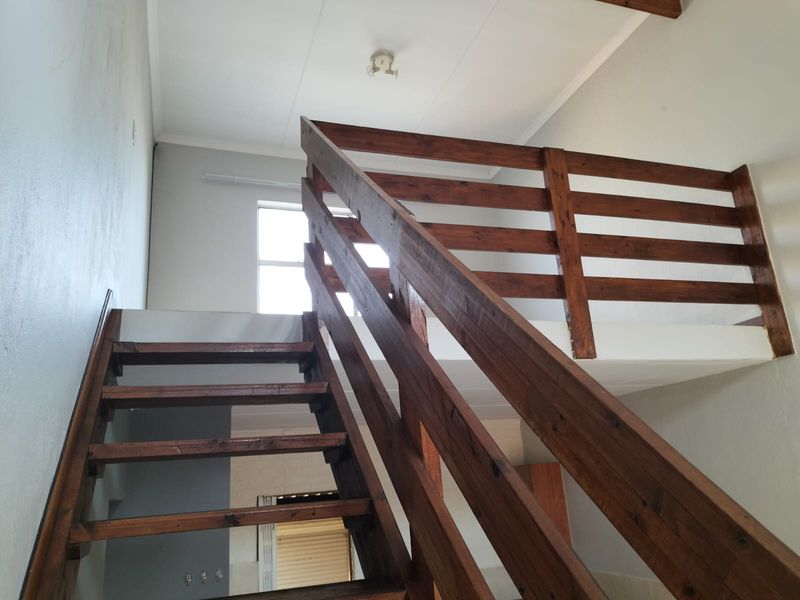 An interior view of an apartment featuring a wooden staircase leading to a mezzanine level with exposed ceiling beams.