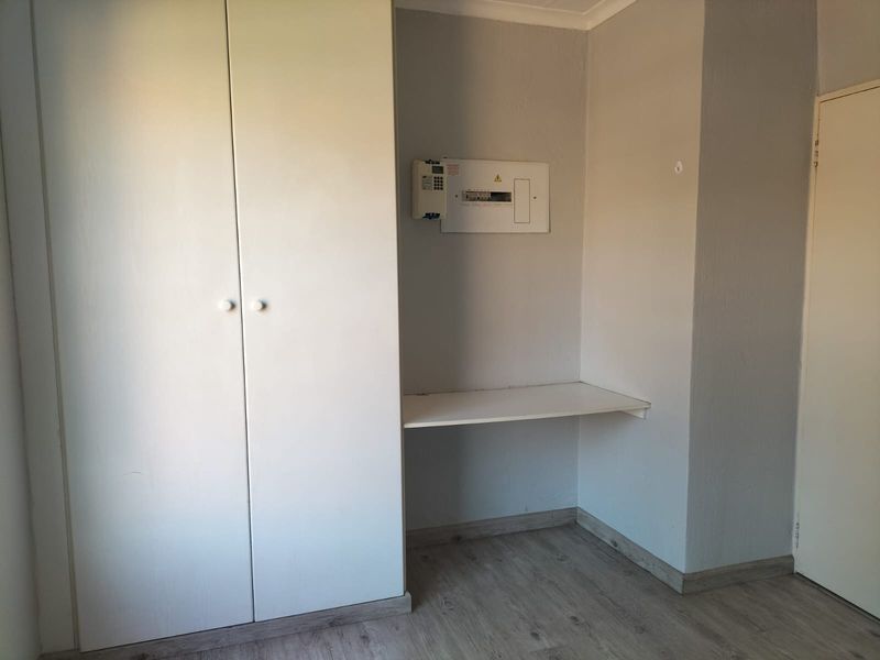 A functional utility space featuring a built-in cupboard, fixed shelving, and an accessible electrical distribution board, finished with modern laminate flooring.