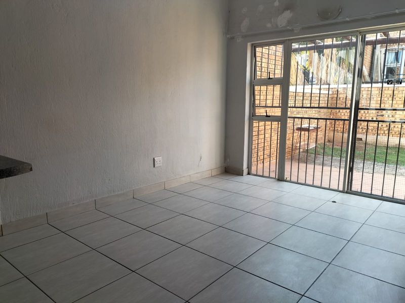 An empty living room featuring tiled flooring and a sliding glass door with security gate, providing direct access to an outdoor patio area.