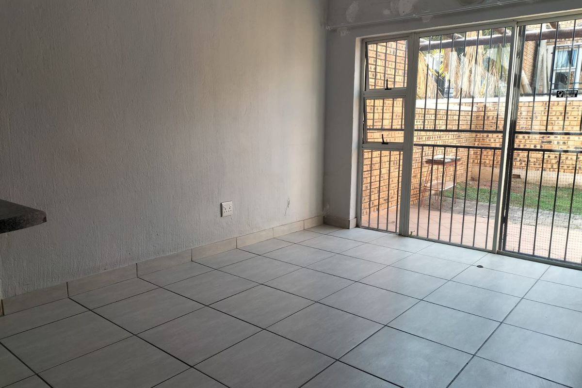 An empty living room featuring tiled flooring and a sliding glass door with security gate, providing direct access to an outdoor patio area.