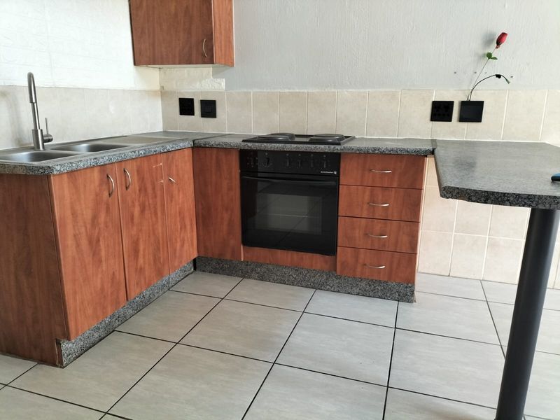 A functional kitchen featuring wood-look cabinetry, granite-style laminate countertops, built-in oven and hob, and a breakfast bar with tiled flooring.