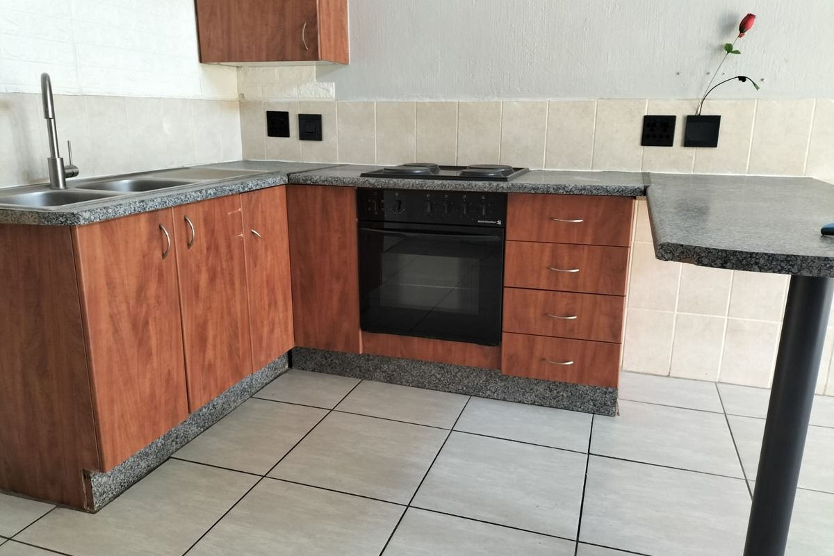 A functional kitchen featuring wood-look cabinetry, granite-style laminate countertops, built-in oven and hob, and a breakfast bar with tiled flooring.