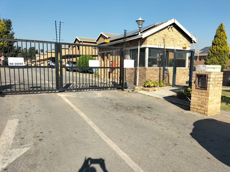 Secure gated entrance to the apartment complex featuring a brick guardhouse, electric fencing, and solar-powered infrastructure.