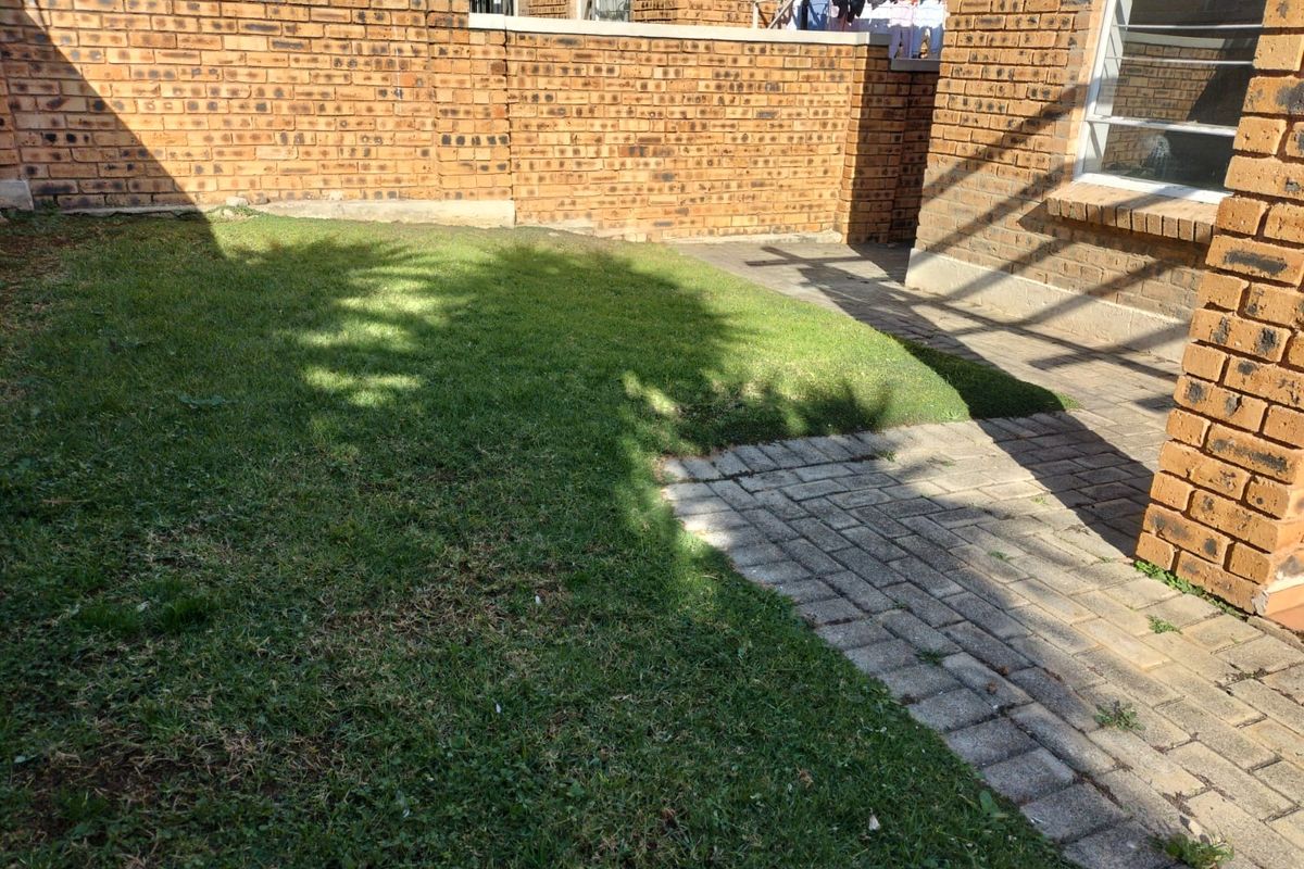 A private rear garden area featuring a brick boundary wall, a paved walkway, and a small lawn.
