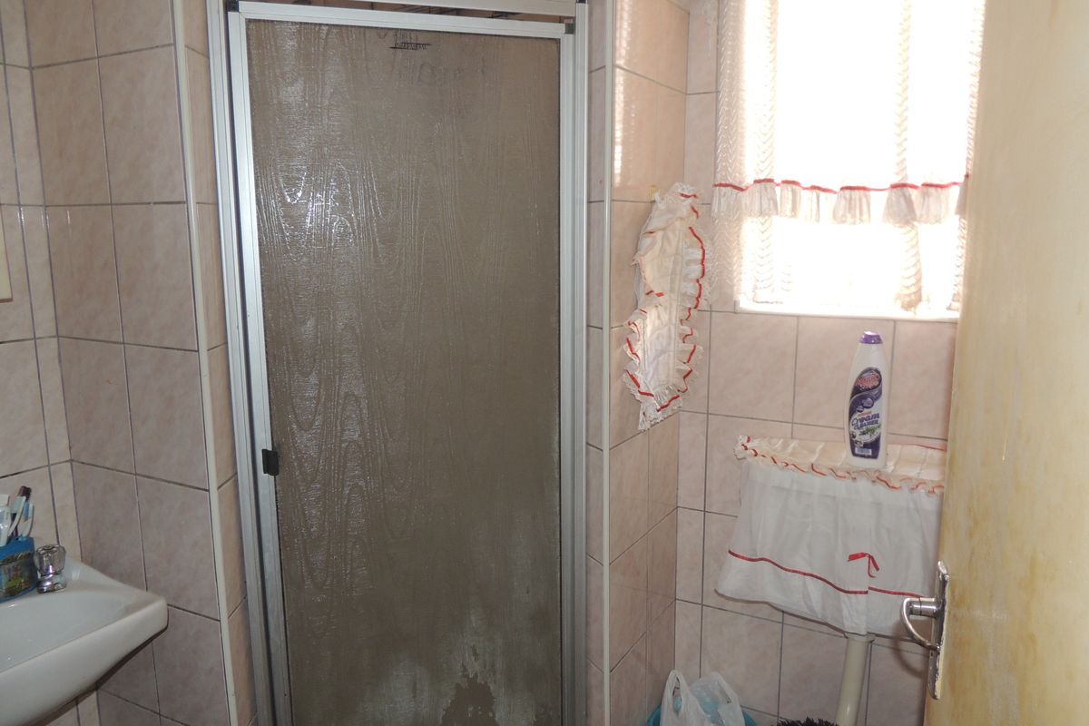 A compact bathroom featuring a shower enclosure, wall tiling, and a wall-mounted washbasin, requiring cosmetic updates to improve its overall condition.