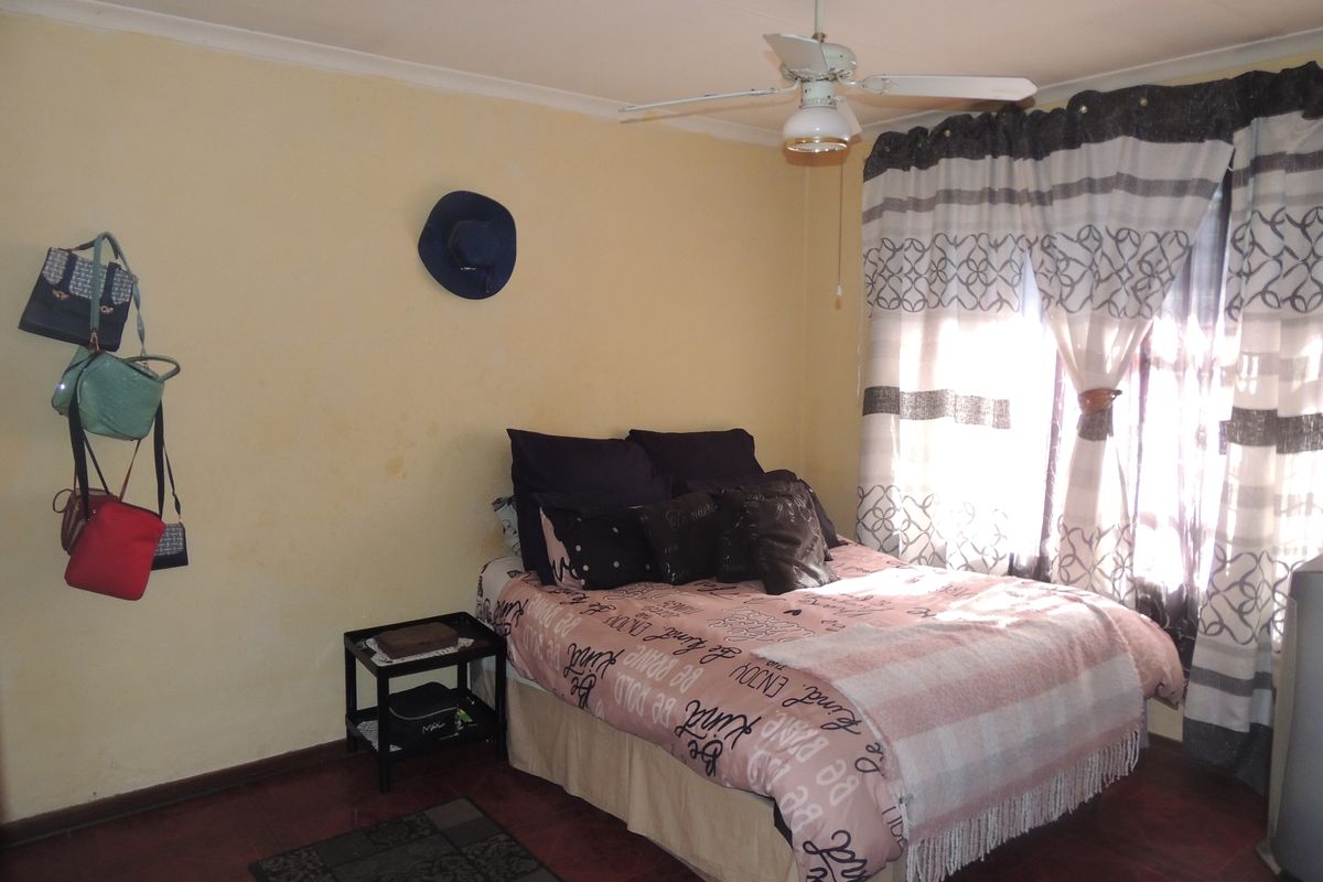 A bedroom featuring tiled flooring and a ceiling fan, currently showing signs of wall discoloration and wear.