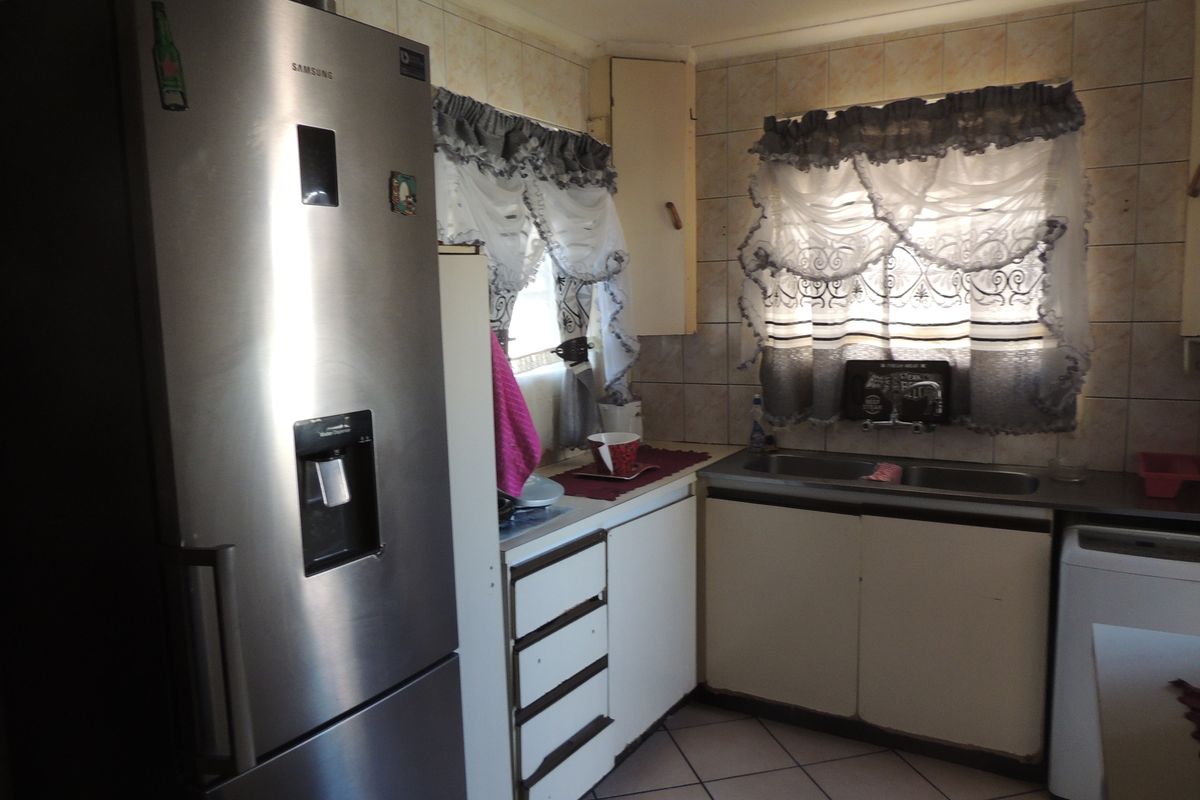 A functional kitchen featuring built-in cabinetry, a double basin sink, and tiled splashbacks, offering a practical layout with potential for modern updates.