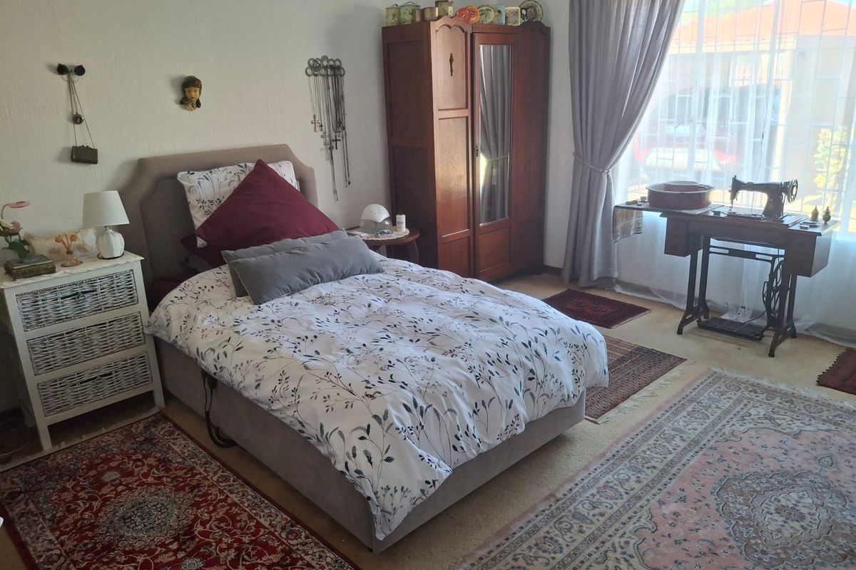A well-lit bedroom featuring neutral wall finishes, carpeted flooring, and large windows with curtain treatments, offering a comfortable and functional living space.