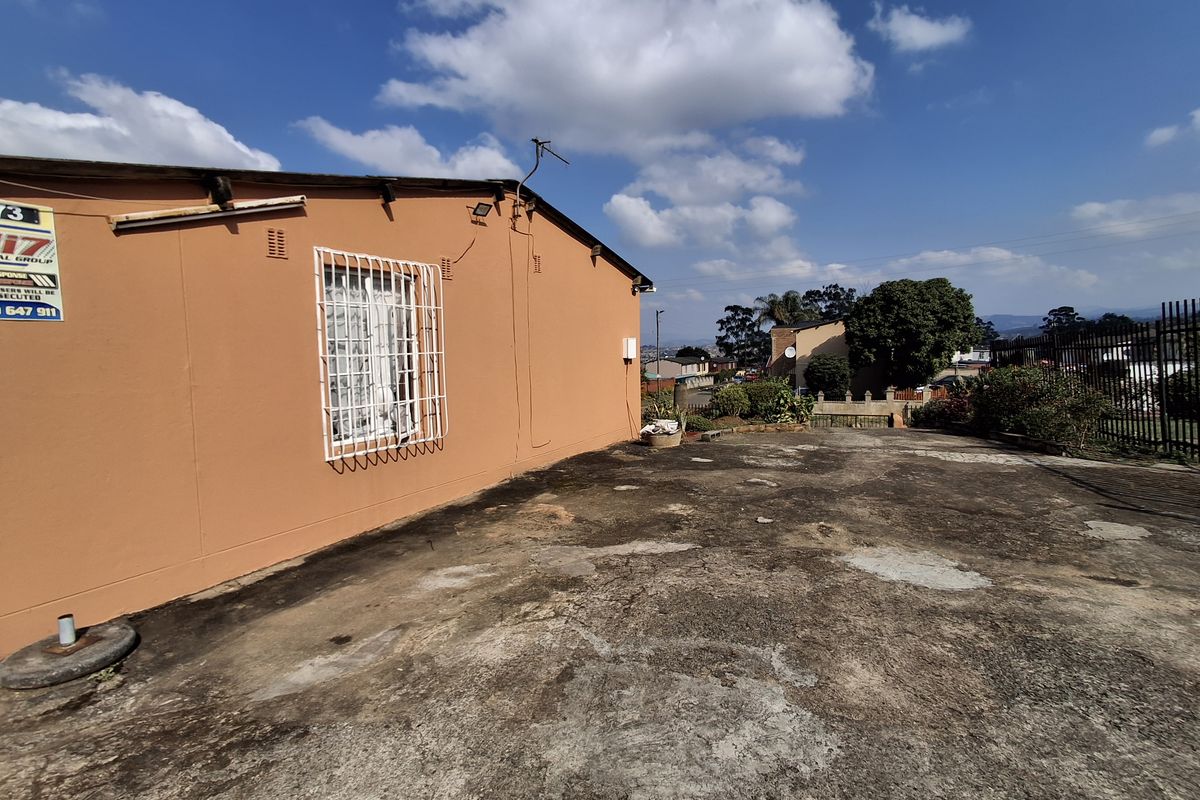Exterior view of the property showing a side yard with a concrete area and a security-grilled window on the orange-painted building facade.