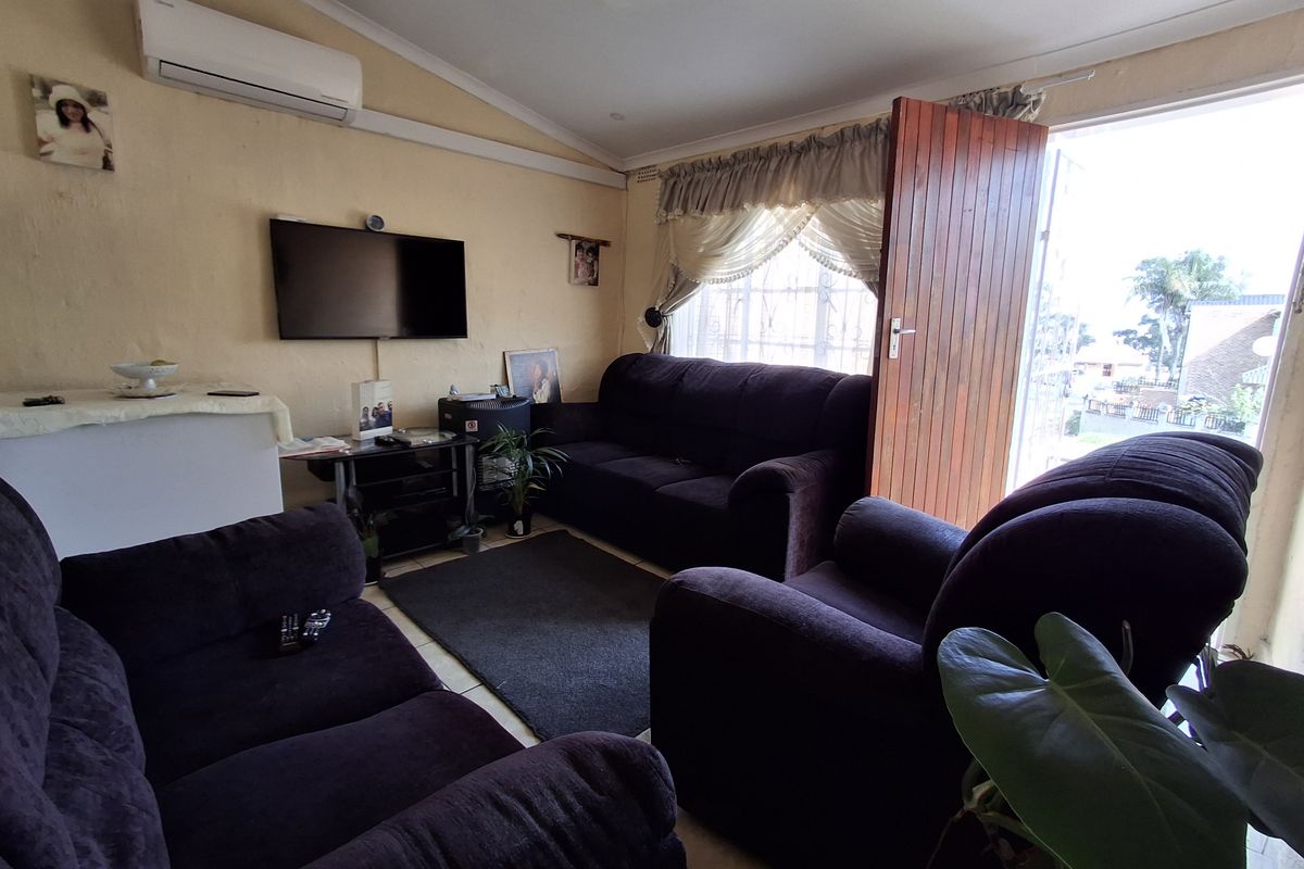 A comfortable living room featuring a wall-mounted air conditioning unit, tiled flooring, and direct access to the exterior through a wooden door.