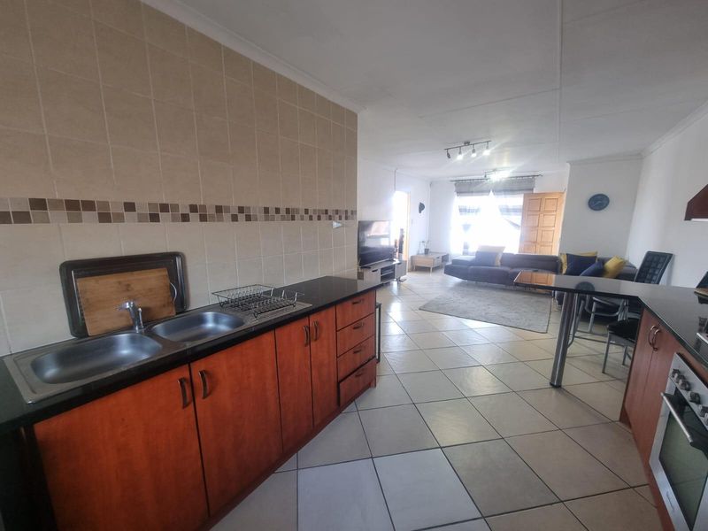 Open-plan living area featuring a kitchen with dark countertops, wooden cabinetry, and tiled flooring, flowing into a comfortable lounge space.