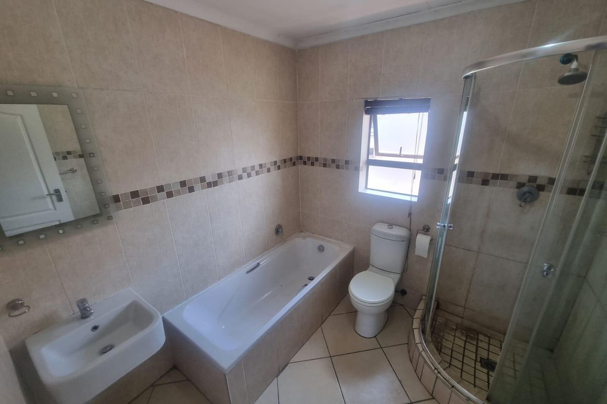 A functional bathroom featuring a bathtub, separate glass-enclosed shower, wall-mounted basin, and tiled finishes throughout.