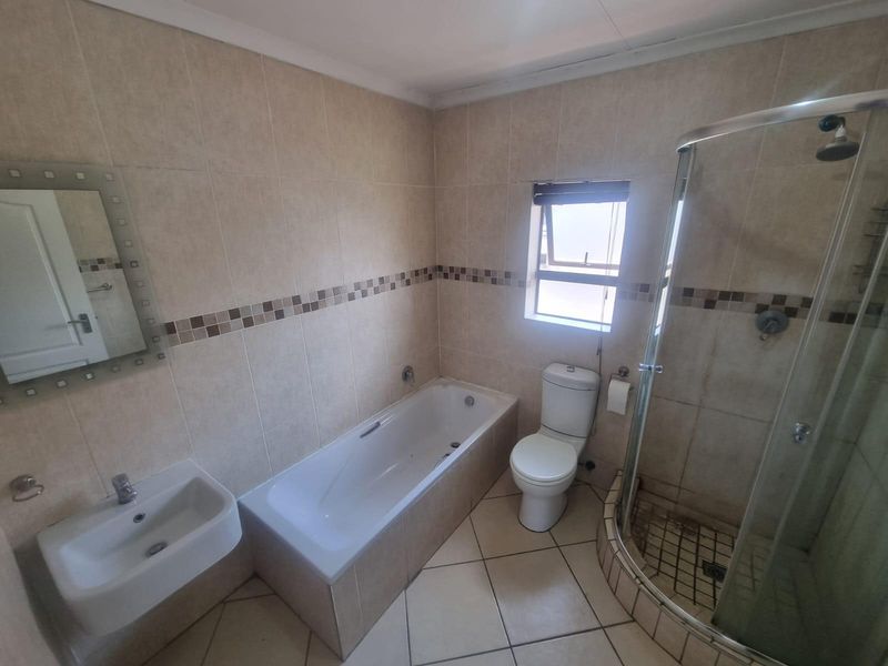 A functional bathroom featuring a bathtub, separate glass-enclosed shower, wall-mounted basin, and tiled finishes throughout.