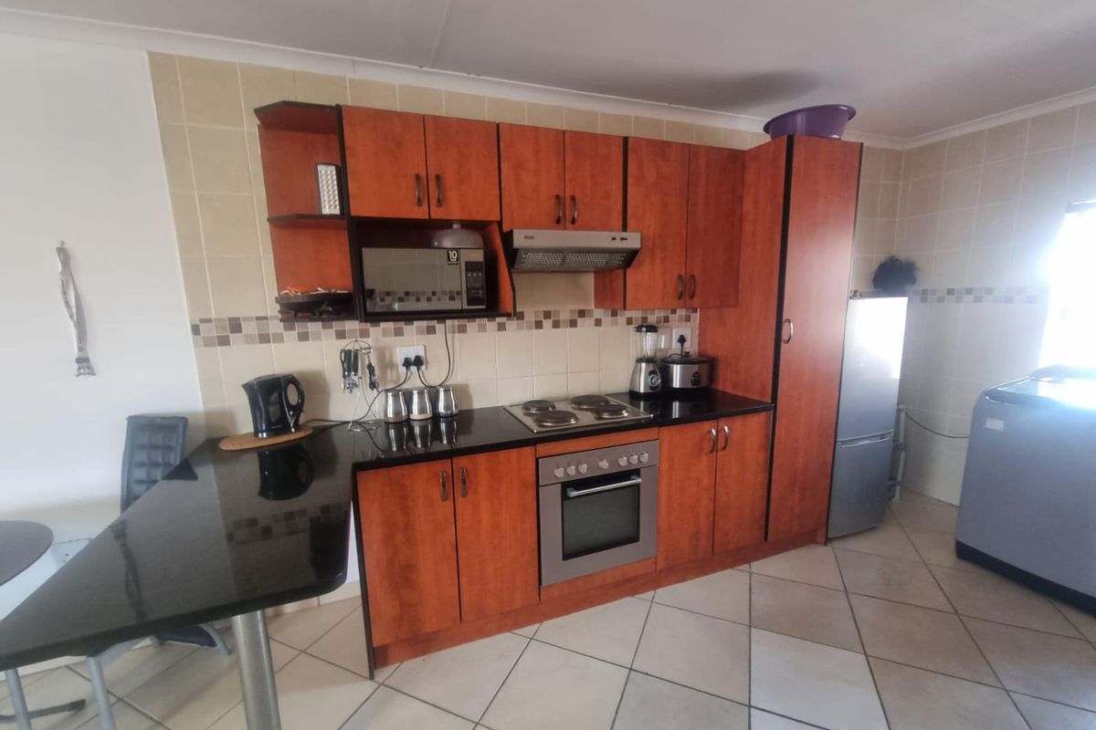 A functional kitchen featuring wooden cabinetry, black granite countertops, a built-in oven, electric hob, and tiled flooring.