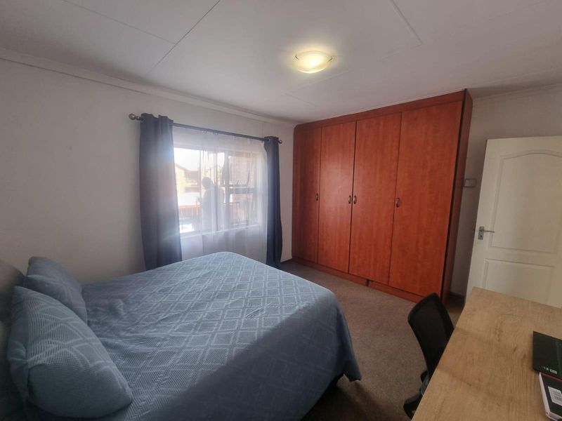 A bedroom featuring built-in wooden wardrobes, carpeted flooring, and a window providing natural light.