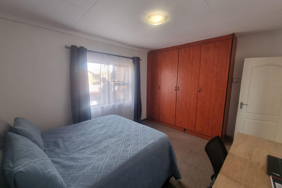 A bedroom featuring built-in wooden wardrobes, carpeted flooring, and a window providing natural light.