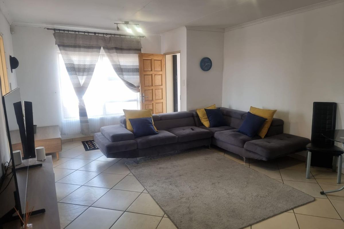 A functional living room featuring tiled flooring, neutral walls, and natural light through a window with a door leading to an exterior area.