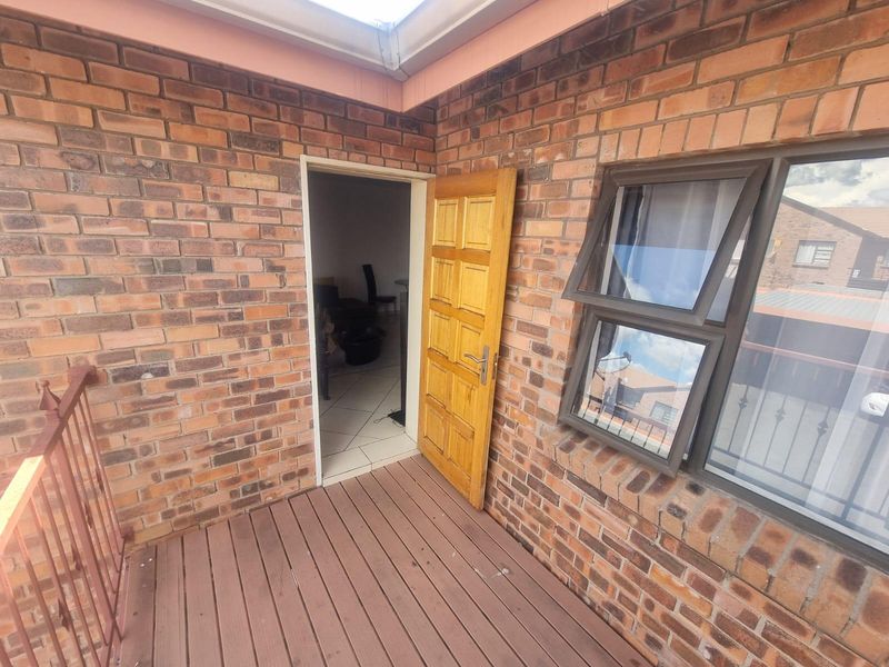 A private balcony area featuring face-brick exterior walls, a timber entrance door, and a top-hung window, providing access to the interior living space.