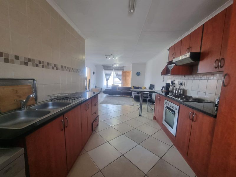 Open-plan kitchen and living area featuring wooden cabinetry, built-in oven, hob, extractor fan, and tiled flooring throughout the space.