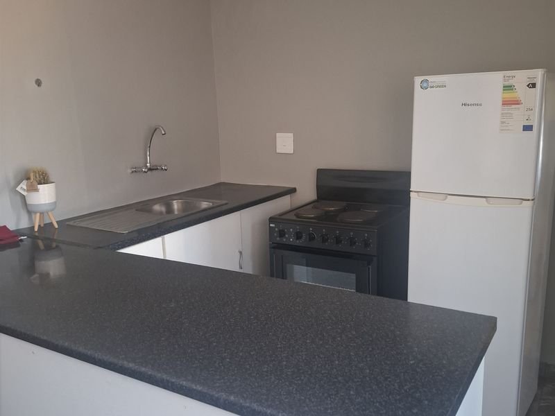 Compact kitchen featuring laminate countertops, stainless steel sink, and a freestanding electric stove with neutral wall finishes.