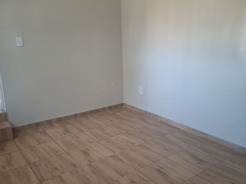 A bright, empty living area featuring neutral painted walls, coved cornicing, and modern wood-look ceramic floor tiles.