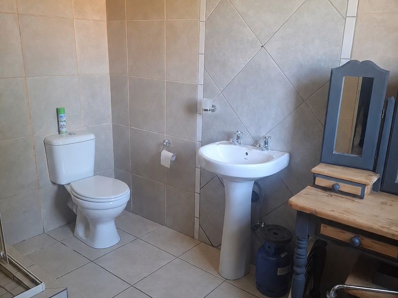 A functional bathroom featuring a pedestal basin, toilet, and neutral ceramic tiling throughout, providing a clean and practical space.
