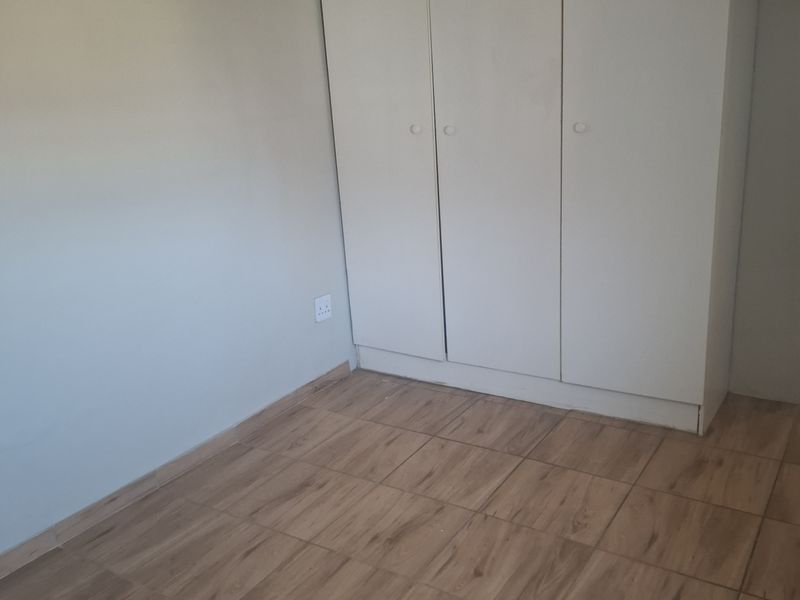 A clean, empty bedroom featuring wood-look tiled flooring and a white built-in wardrobe, offering a neutral canvas for personalization.