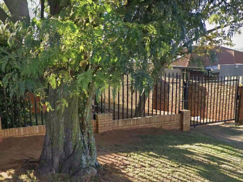 Front garden area featuring a mature tree, brick boundary wall, and metal security fencing with a gate.