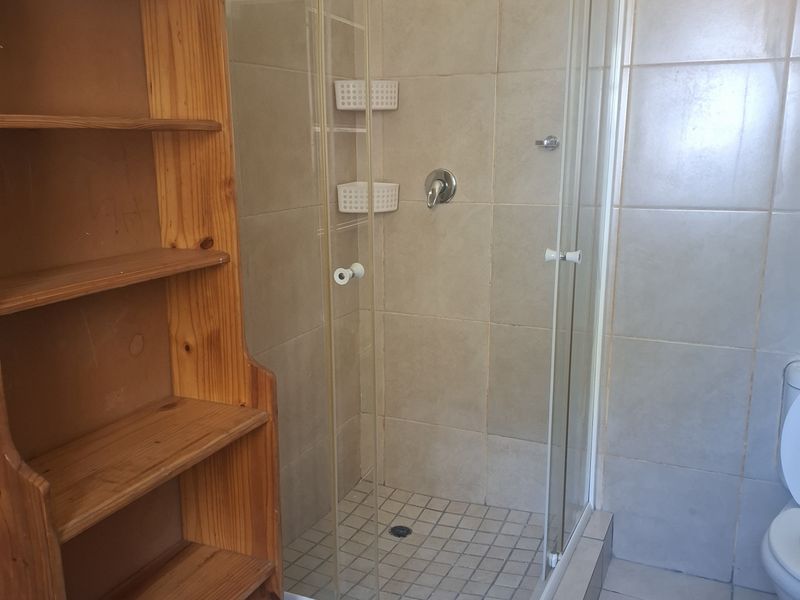 A functional bathroom featuring a tiled shower enclosure with a modern shower head and standard ceramic wall and floor tiling.