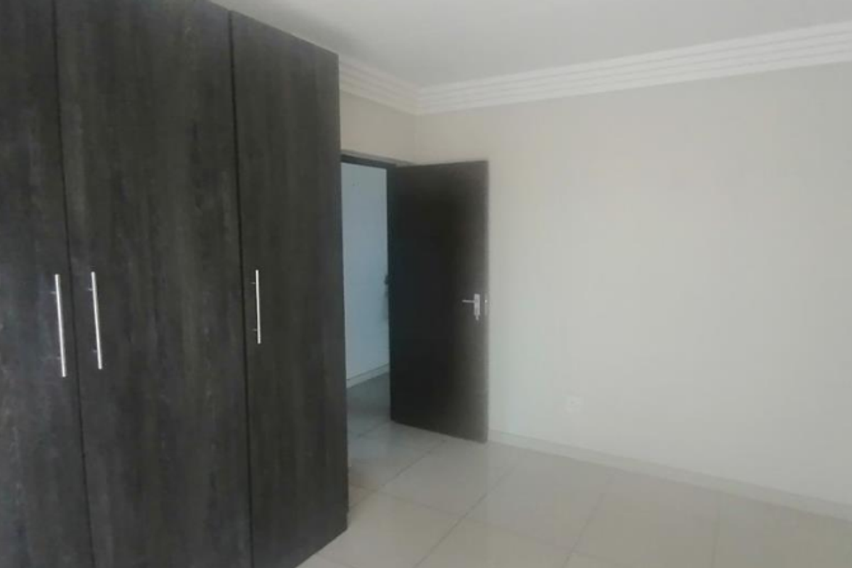 A clean, empty bedroom featuring neutral tiled flooring, white walls, decorative ceiling cornicing, and dark wood-finish built-in cupboards.