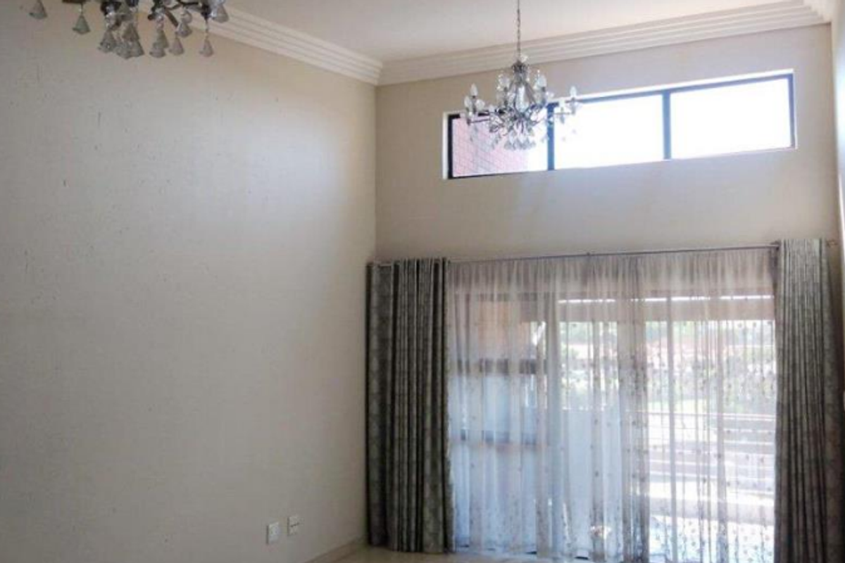 Spacious living area featuring double volume ceilings, elegant crystal chandeliers, and large sliding glass doors that provide ample natural light.
