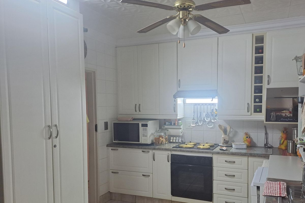 A functional kitchen featuring white cabinetry, integrated oven, hob, extractor fan, and a ceiling fan, with a tiled backsplash and built-in wine storage.