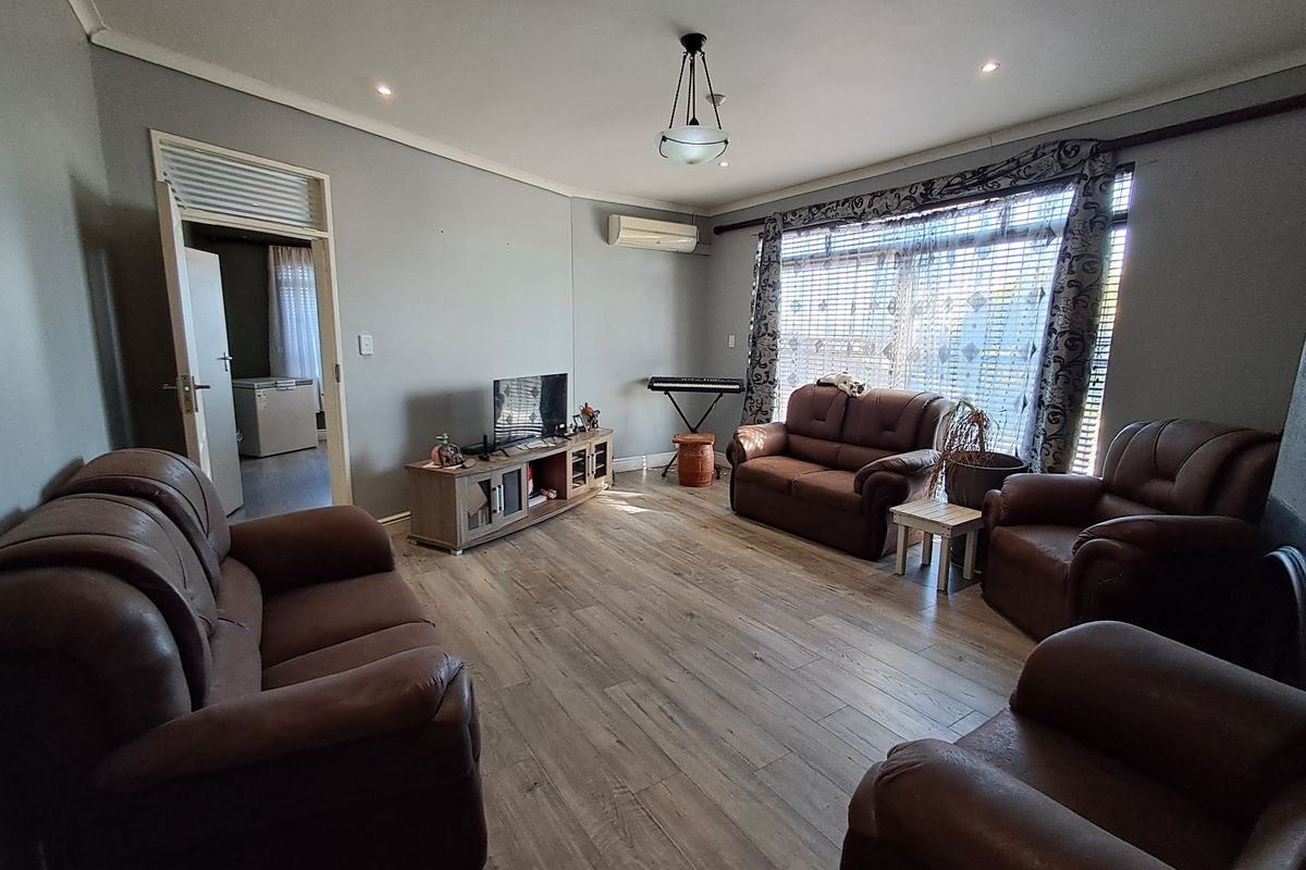 A spacious living room featuring light-toned laminate flooring, neutral wall finishes, an integrated air conditioning unit, and ample natural light through large windows.