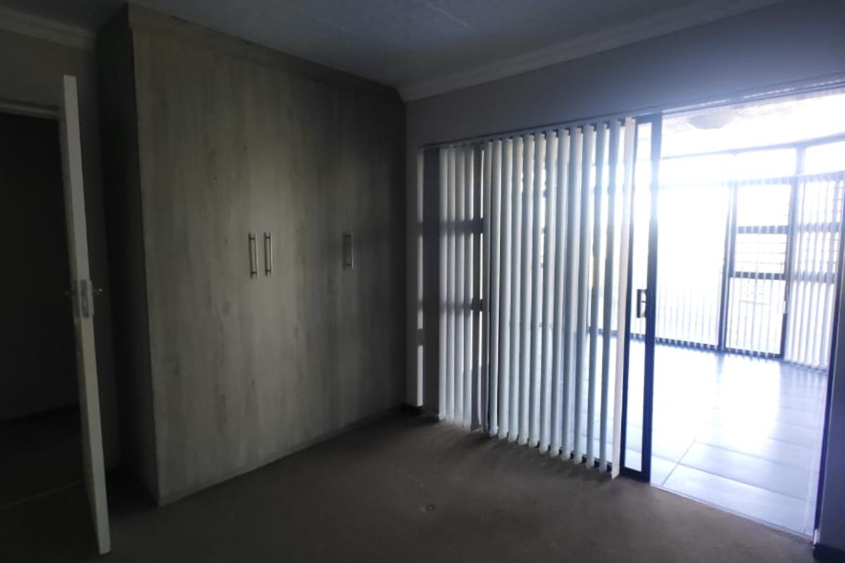 A spacious bedroom featuring built-in cupboards, carpeted flooring, and a sliding glass door leading to an adjacent patio area.