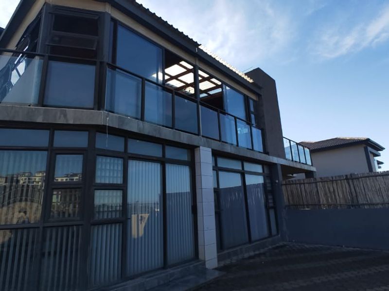 Rear view of a multi-story residential property featuring large glass sliding doors, a balcony with a glass balustrade, and a paved outdoor area.