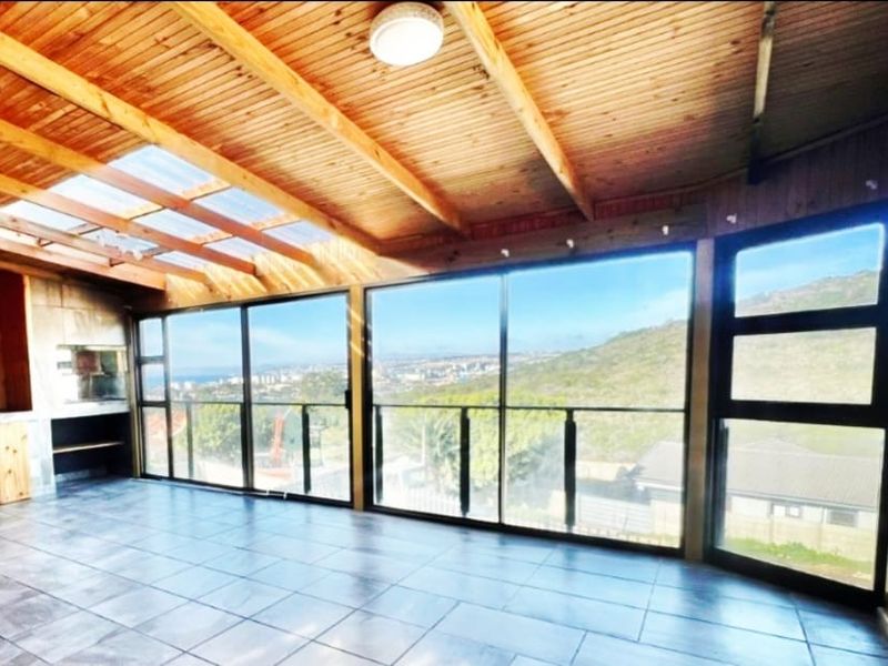Spacious enclosed patio featuring a timber-clad ceiling, skylight, built-in braai, and expansive glass windows offering panoramic views.