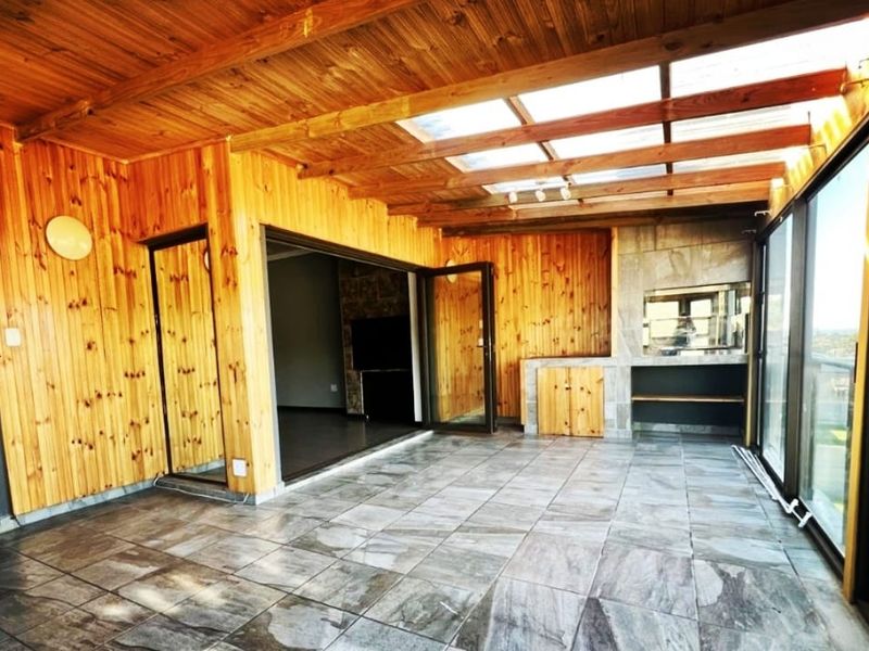 Spacious covered patio featuring timber paneling, a skylight, tiled flooring, and a built-in braai, offering a versatile outdoor entertainment area.