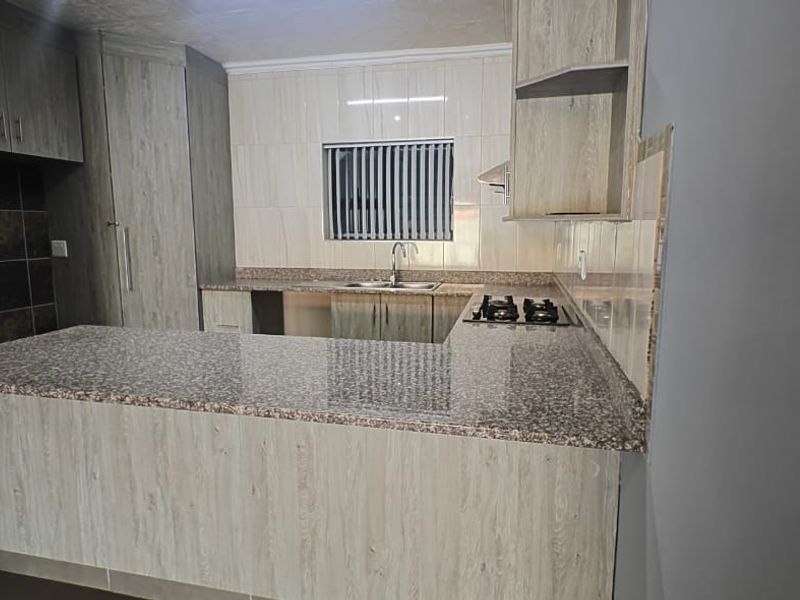 Modern kitchen featuring light wood-grain cabinetry, granite countertops, a gas hob, and a tiled backsplash, offering a clean and functional workspace.