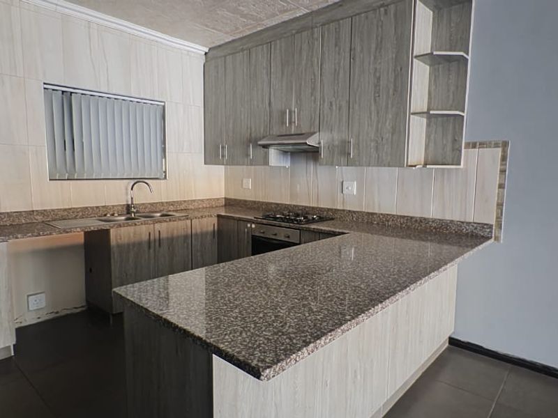 Modern kitchen featuring granite countertops, built-in cabinetry, a gas hob with extractor fan, and tiled finishes throughout.