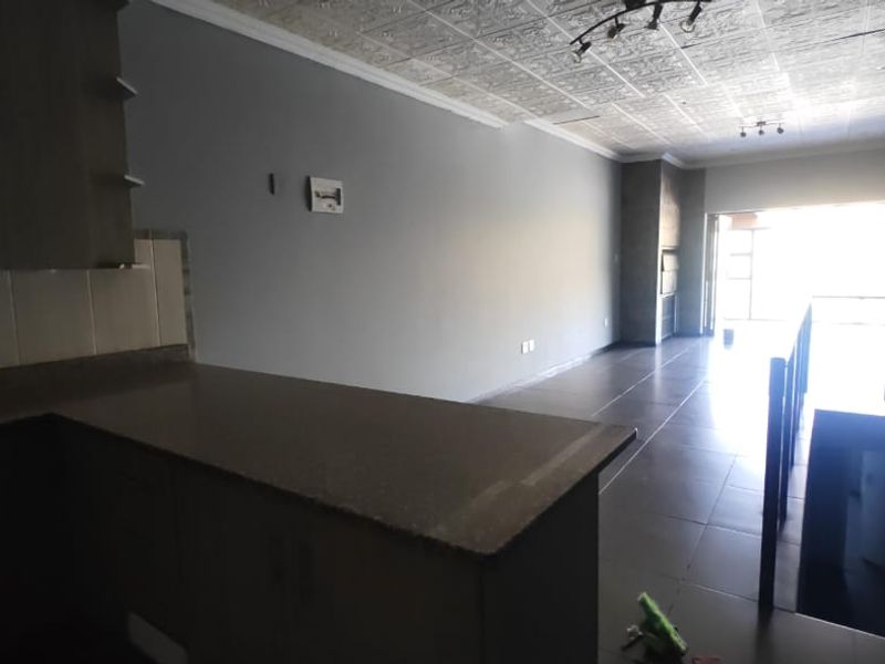 Spacious open-plan living area featuring a modern kitchen with stone countertops, tiled flooring, and a built-in fireplace, leading to an outdoor balcony.