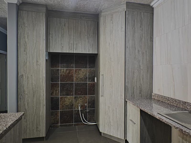 A functional kitchen featuring wood-look built-in cabinetry, granite countertops, a stainless steel sink, and tiled splashbacks with a neutral aesthetic.