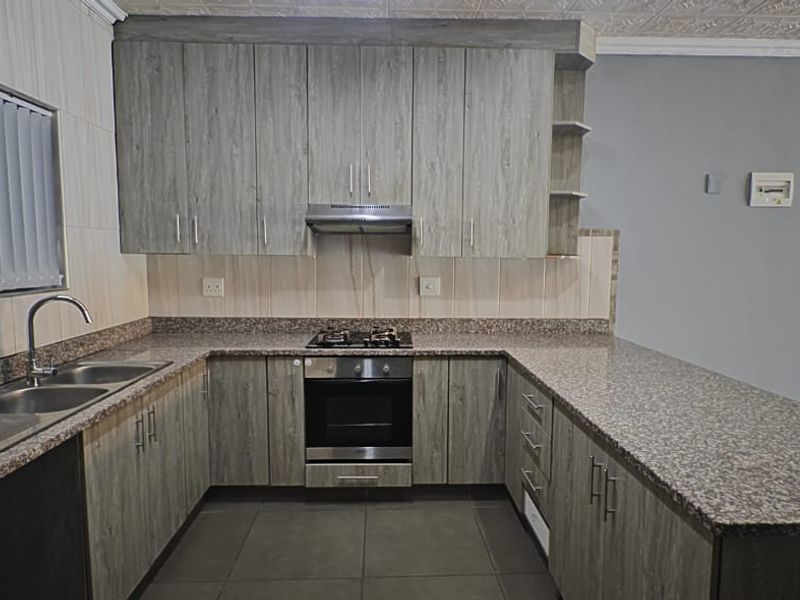 Modern kitchen featuring granite countertops, built-in oven, gas hob, extractor fan, and ample laminate cabinetry with a breakfast bar.