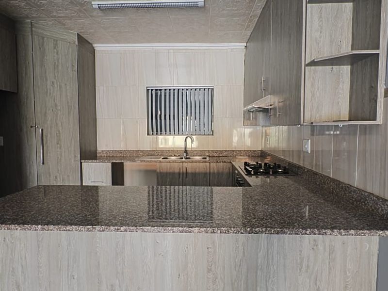 Modern kitchen featuring granite countertops, ample built-in cabinetry, a gas hob with extractor fan, and a functional breakfast bar layout.