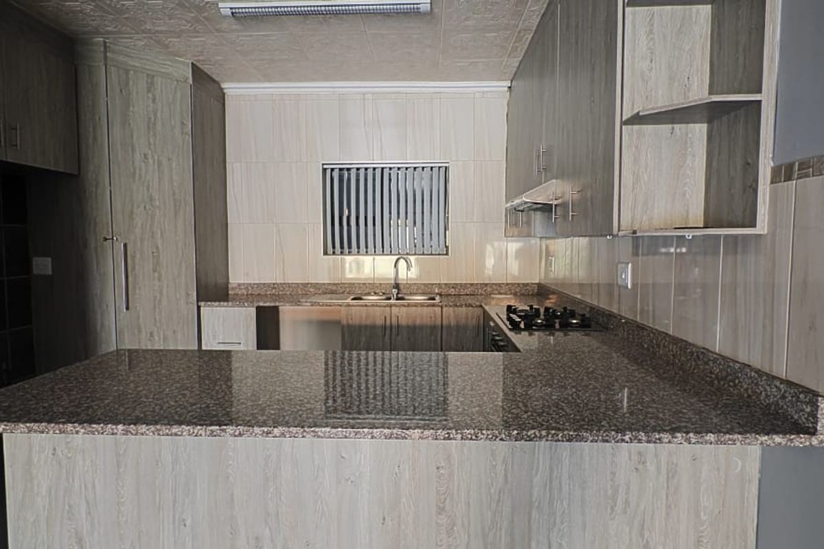 Modern kitchen featuring granite countertops, ample built-in cabinetry, a gas hob with extractor fan, and a functional breakfast bar layout.