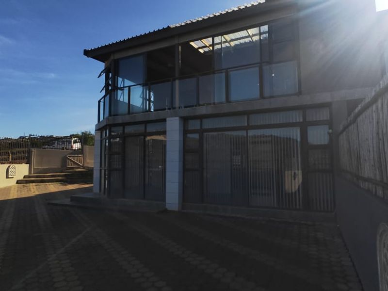 Rear exterior view of the property featuring a paved driveway, a balcony with metal railings, and large sliding glass doors.